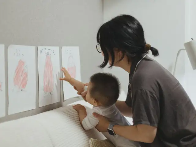 赤ちゃんを支えて、壁に貼った絵を一緒に見るお母さん